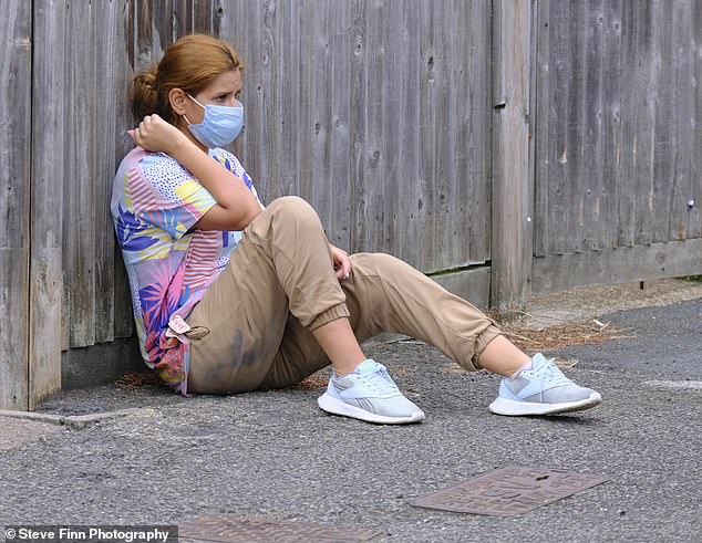 A woman wearing a face mask is seen sitting on the pavement after she crossed the Channel with a group on Friday