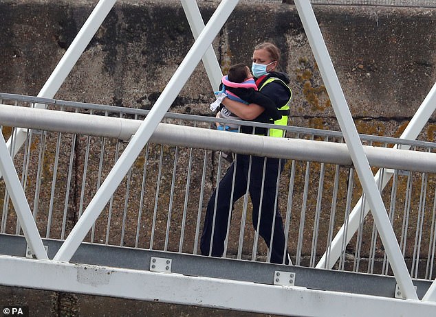 A young child is held by a Border Force officer. Groups of migrants continued to arrive in Dover on Friday