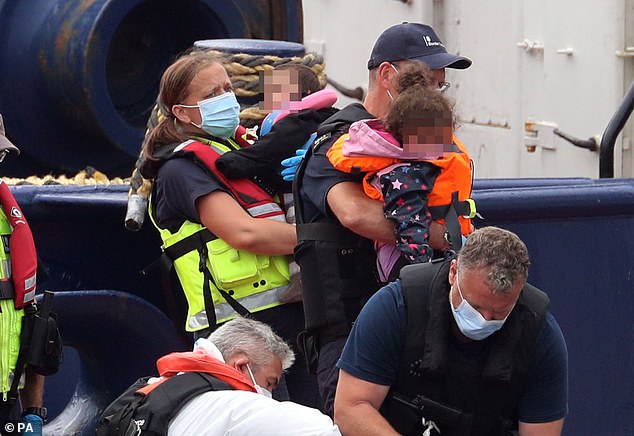 Two young children are carried by officials when they arrive into Dover after crossing the Channel