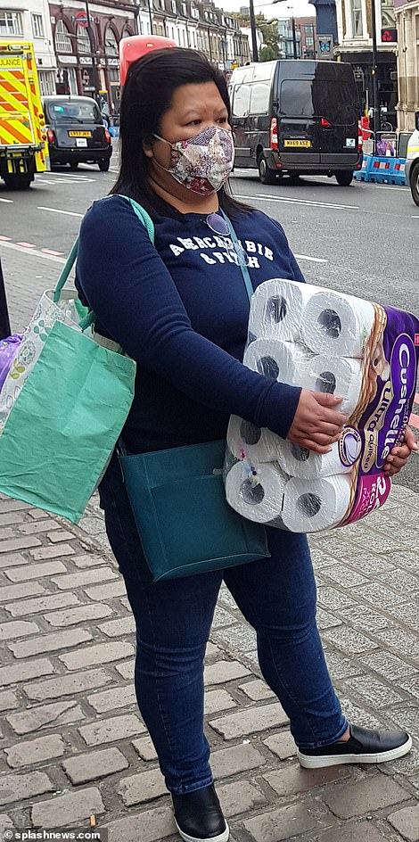 A woman wears a face mask as she leaves a shop in Camden Town with toilet papeer